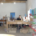 Beth sits behind a computer at a large table in a semi cluttered room, analyzing artifacts