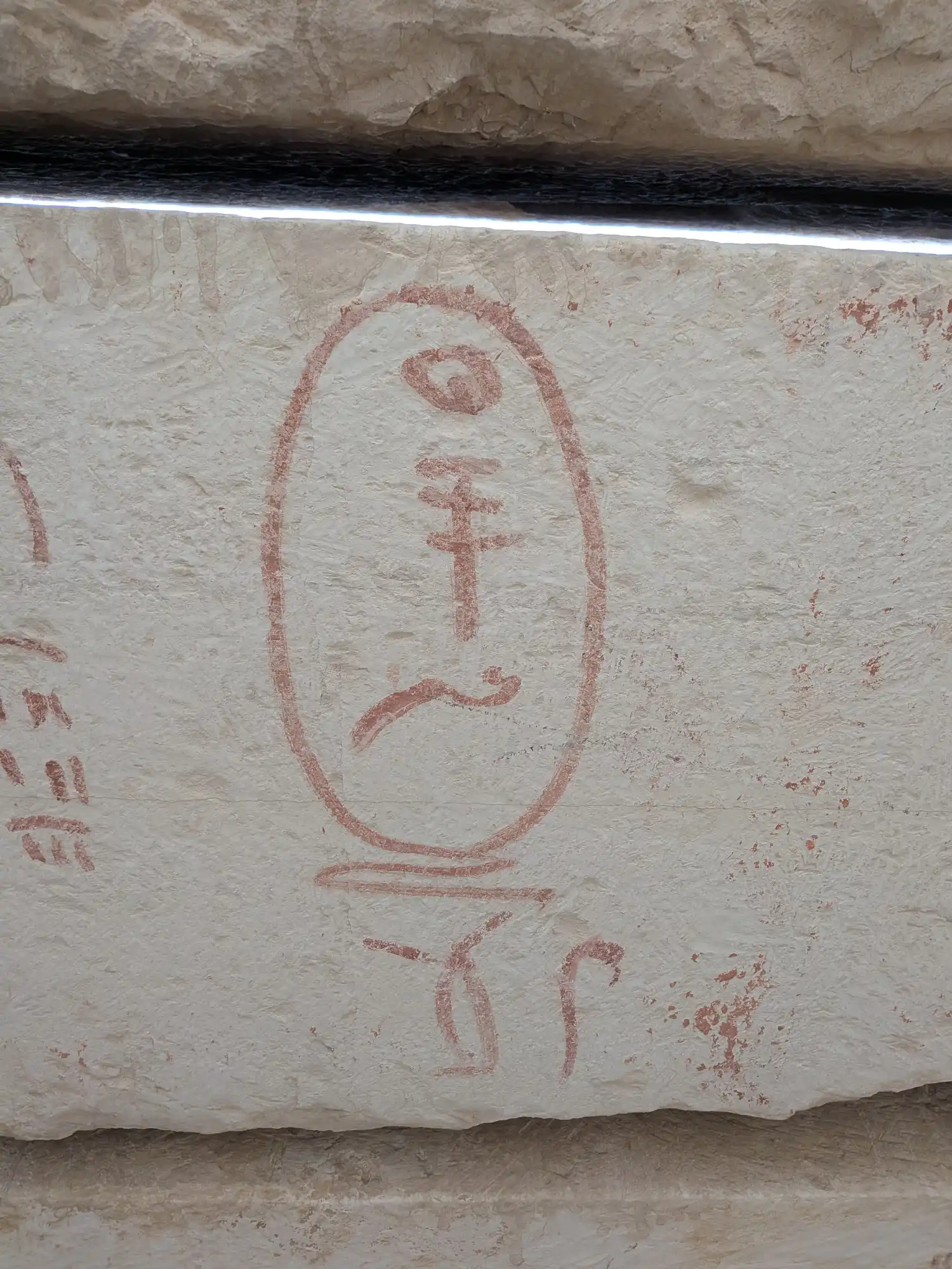 A large white limestone slab with a cartouche marked in red pigment. The cartouche contains three hieroglyphic signs spelling out the name of the pharaoh Djedefre. To the left and below are additional marks/ hieroglyphs.