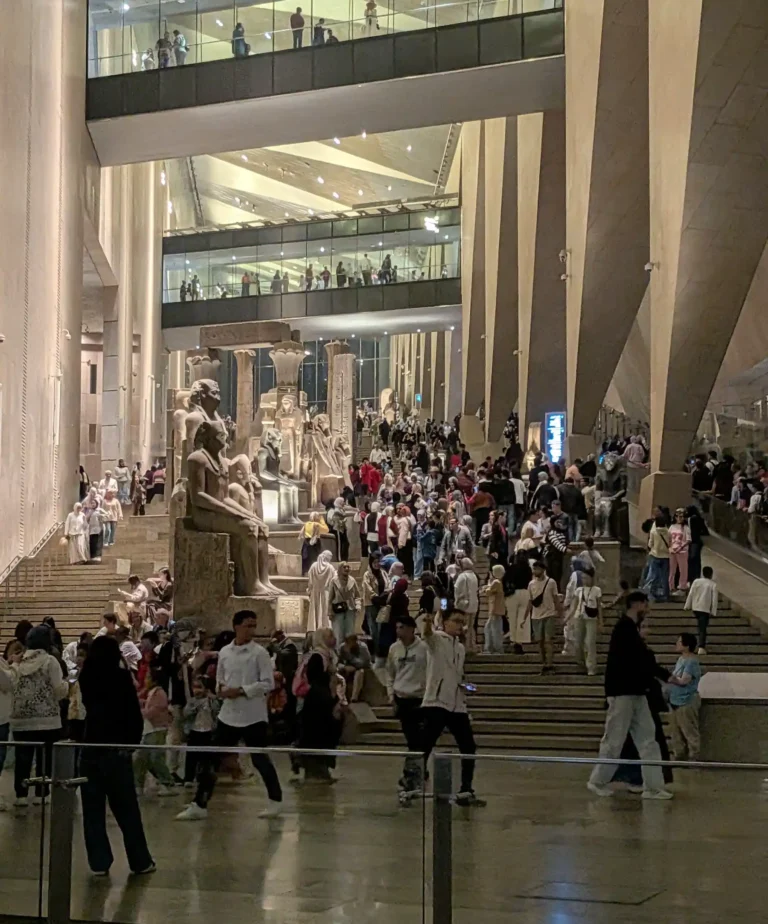 Looking up the grand staircase from the bottom you can see statues all the way up it, but the staircase is flooded with hundreds of people. You can also see people crossing on a walkway above.