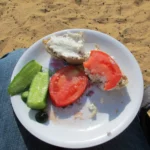 Egyptian Cuisine: 7 surprising things for first-time travelers A white plate balanced on a person's lap in the desert features a rustic meal of aish shams spread with white cheese, fresh tomato slices, and crisp green cucumber spears.