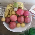 Egyptian Cuisine: 7 surprising things for first-time travelers white ceramic bowl filled with fresh fruit sits on a table, holding a bunch of yellow bananas, several red pomegranates, and small yellow guavas.