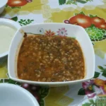 Egyptian Cuisine: 7 surprising things for first-time travelers A square white bowl filled with a thick sauce of spinach and grain cooked in a tomato sauce, sits on a brightly patterned floral tablecloth.