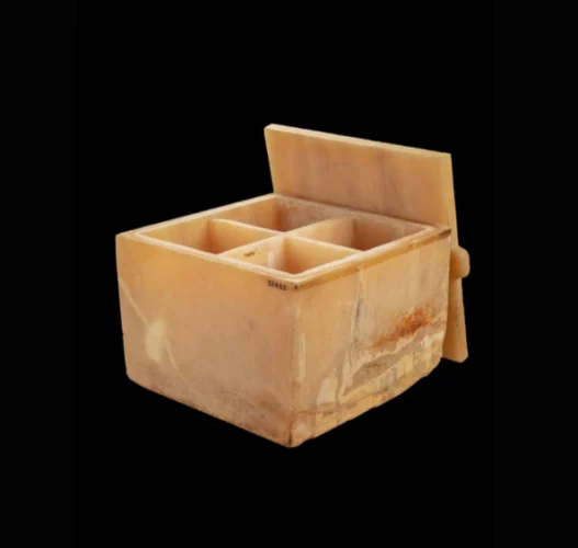 THe alabaster canopic chest is square, the lid is off and placed against the side, revealing that the interior is separated into four sections.