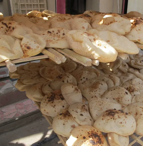 Rows of puffed flatbreads with charred spots sit on two levels of a slatted bamboo drying frame outdoors.
