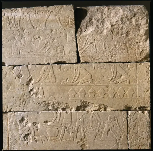 A relief divided into three rows, the middle one has multiple figures kneeling and bending forward over low tables to process grain. Below them, workers stand and sit while using large bowls, jars, vessels to brew beer.
